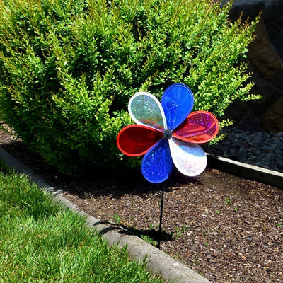 12-inch Patriot Sparkle Flower with red, white, and blue Mylar petals spinning on a fiberglass pole in a sunny garden setting.