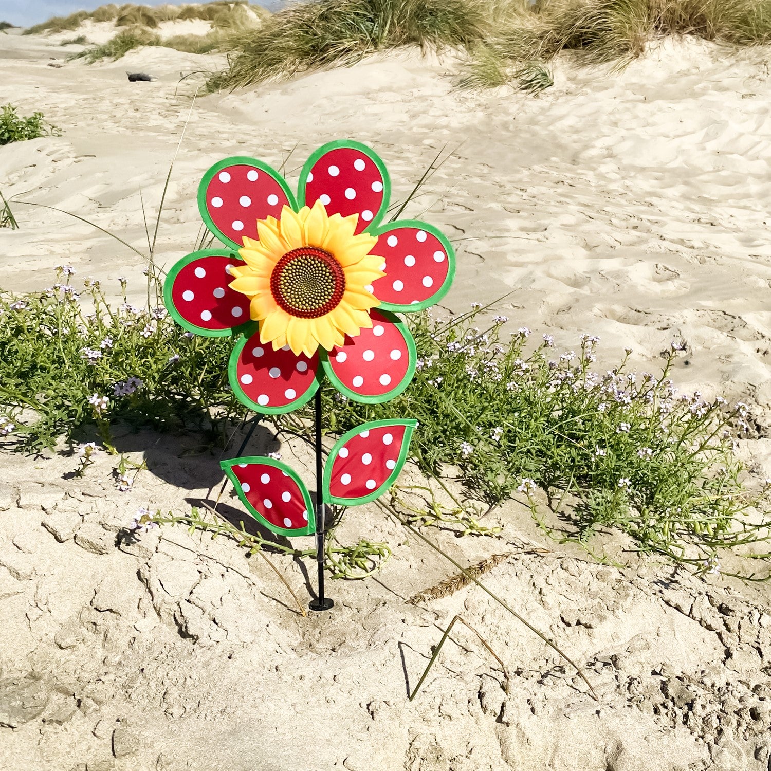 Colorful 12" Polka Dot Sunflower Spinner featuring red and white polka dots, with matching leaves and a sturdy fiberglass pole, displayed outdoors in a garden setting.