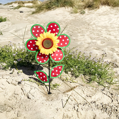 Colorful 12" Polka Dot Sunflower Spinner featuring red and white polka dots, with matching leaves and a sturdy fiberglass pole, displayed outdoors in a garden setting.