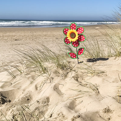 Colorful 12" Polka Dot Sunflower Spinner featuring red and white polka dots, with matching leaves and a sturdy fiberglass pole, displayed outdoors in a garden setting.
