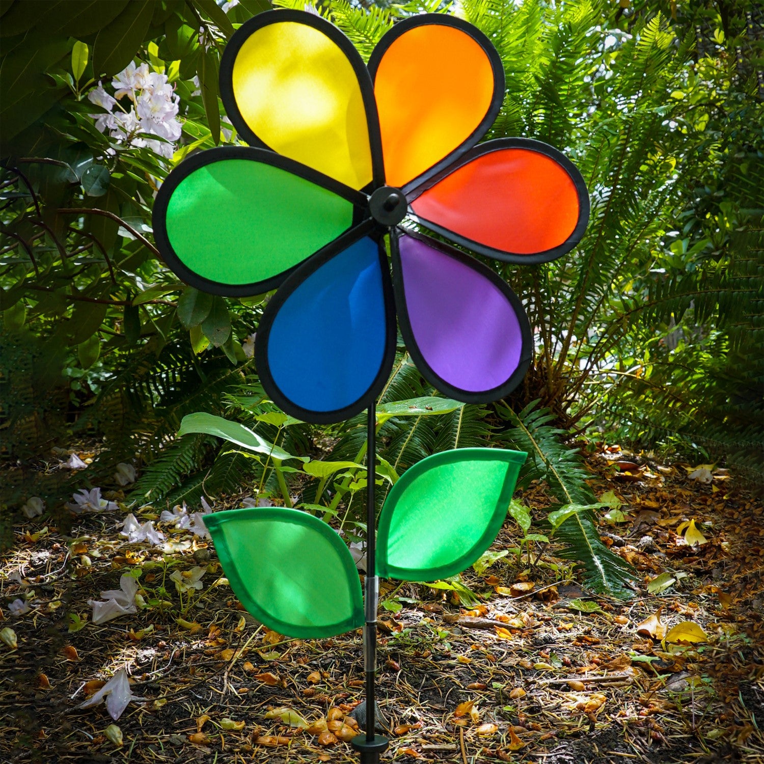12-inch Rainbow Flower Spinner with six colorful petals and leaves on a fiberglass pole, spinning in the breeze in a garden setting.