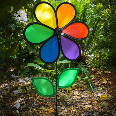 12-inch Rainbow Flower Spinner with six colorful petals and leaves on a fiberglass pole, spinning in the breeze in a garden setting.