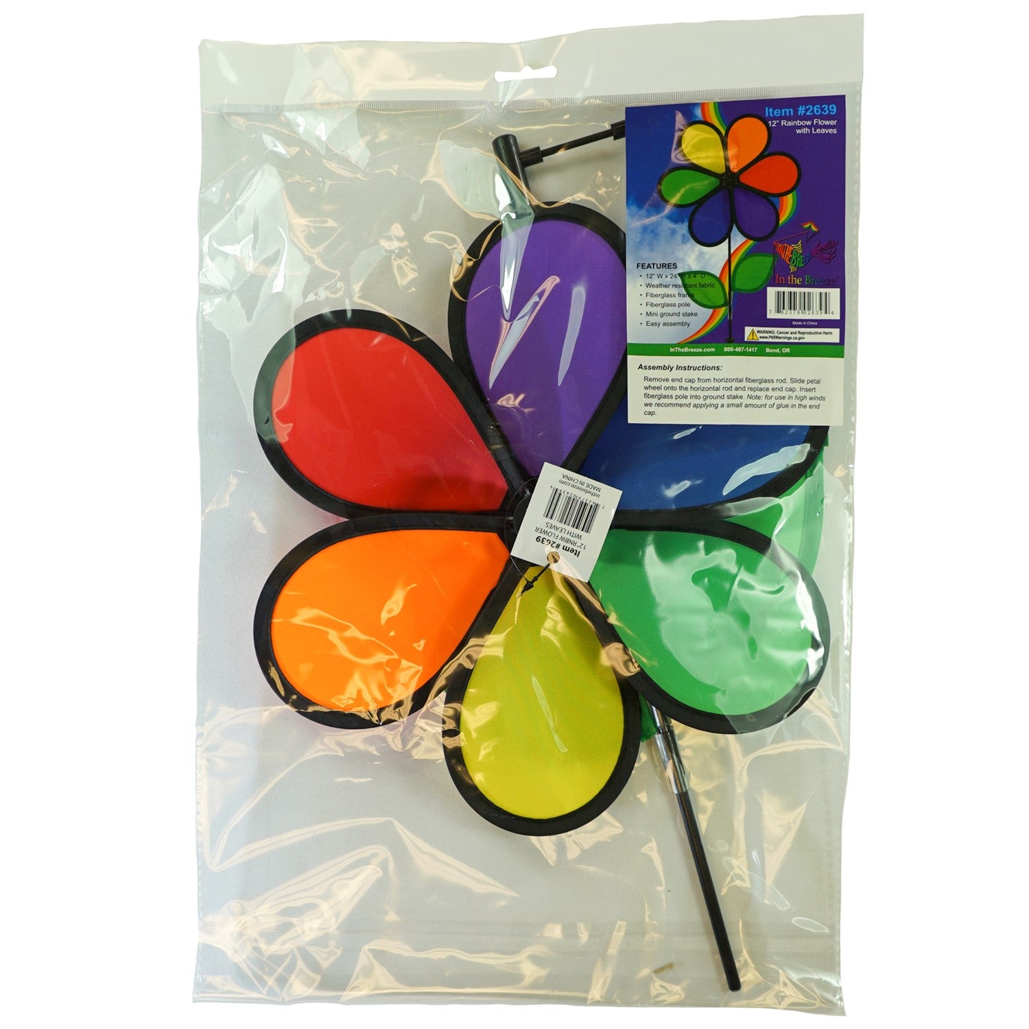 12-inch Rainbow Flower Spinner with six colorful petals and leaves on a fiberglass pole, spinning in the breeze in a garden setting.