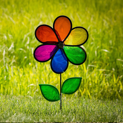 12-inch Rainbow Sparkle Flower Spinner featuring six colorful Mylar petals and green leaves on a fiberglass pole in a garden setting.