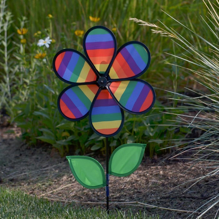 12-inch Rainbow Stripe Flower Spinner with vibrant petals and two leaves attached to a fiberglass pole, spinning in a garden setting.