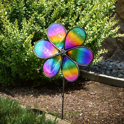 12' Rainbow Whirl Flower Spinner with dazzling multi-colored petals spinning on a fiberglass pole in a garden setting.
