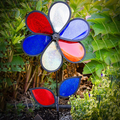 12-inch red, white, and blue sparkle flower spinner rotating in a garden, showcasing its Mylar petals and sturdy fiberglass pole.