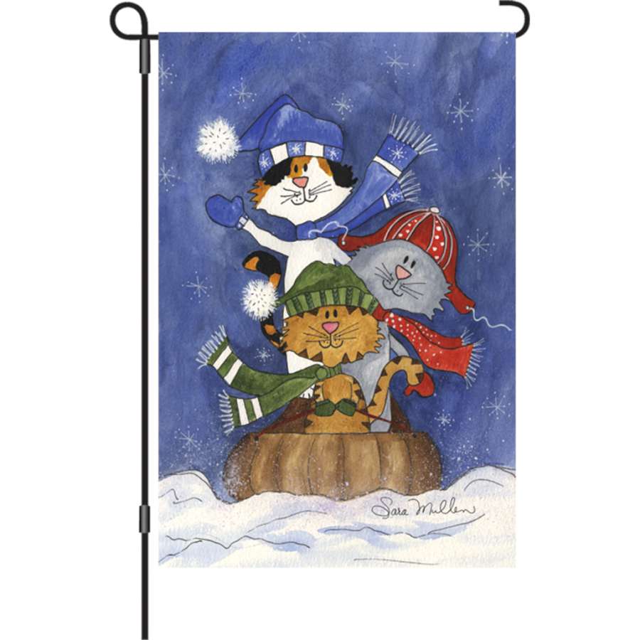 12-inch Sledding Friends garden flag featuring cats sledding in a winter scene, elegantly illuminated for nighttime display in a garden setting.