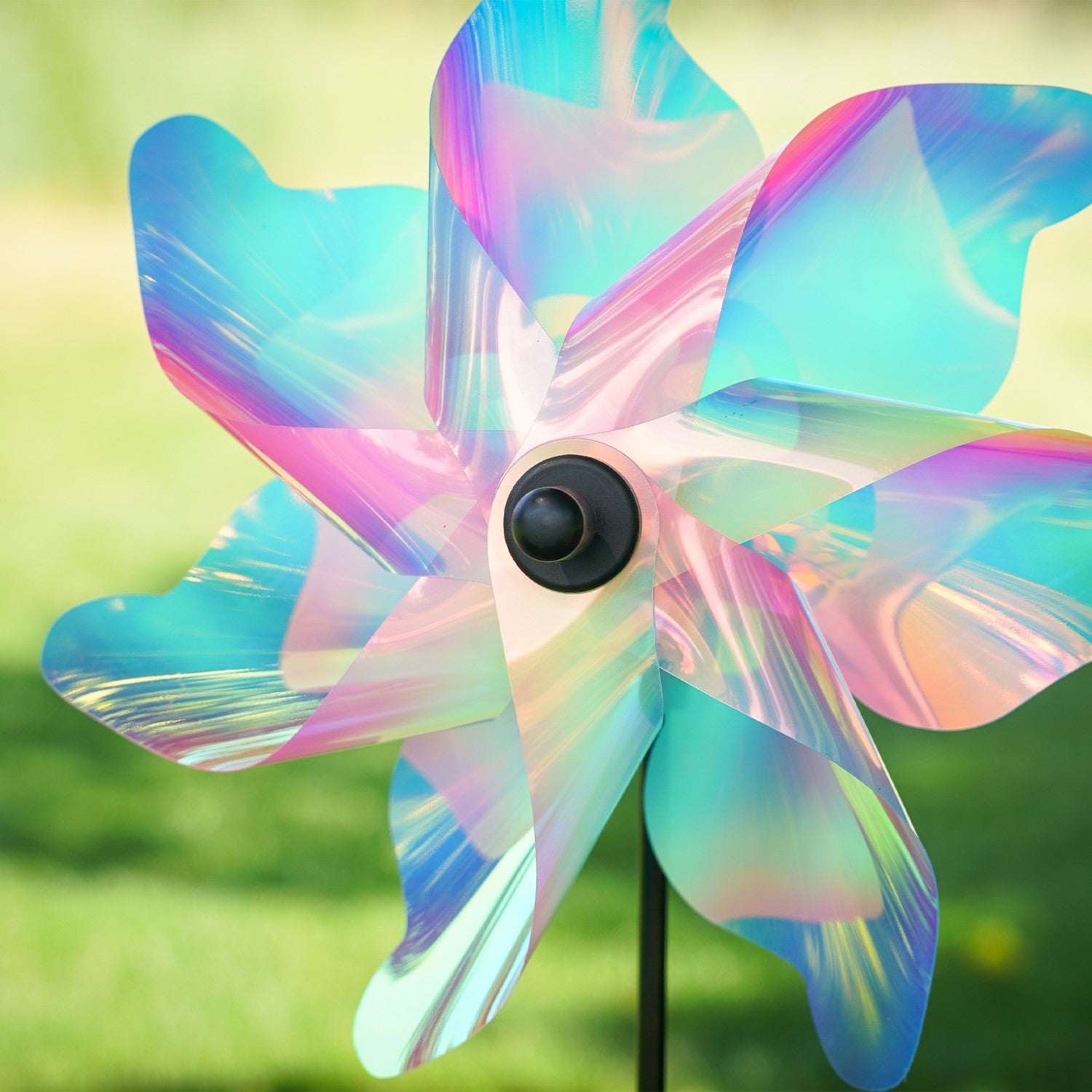12-inch Striped Iridescent Pinwheel Spinner with pastel striped Mylar petals, displayed on a fiberglass pole in a blooming flower garden.