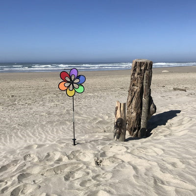 Colorful 12" Rainbow Windee Wheelz Spinner with petal design, set against a bright blue sky in a garden setting, showcasing its vibrant hues.