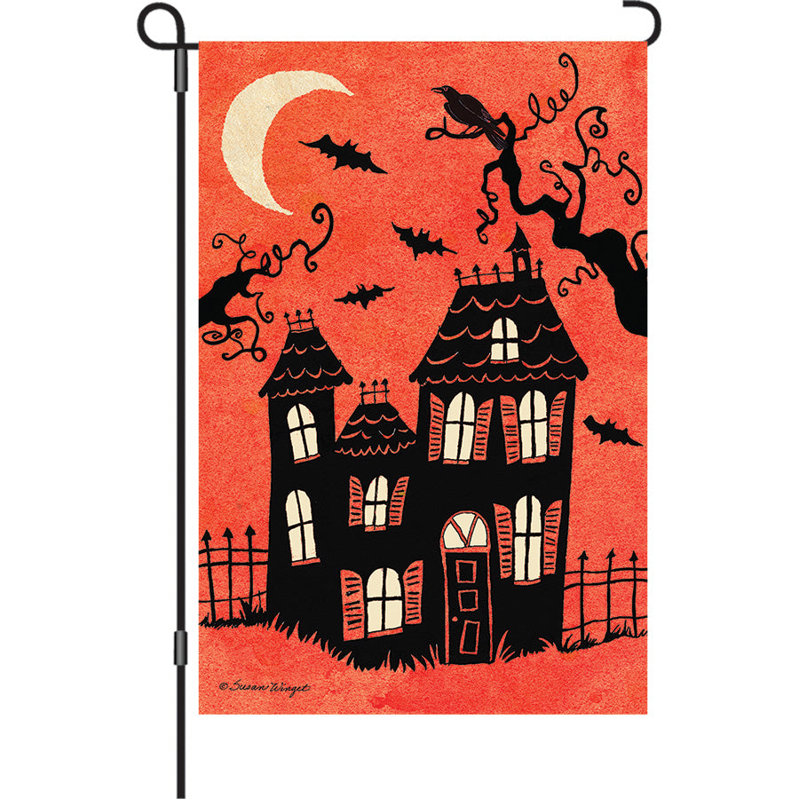 13 in. Elite Oversized Garden Flag featuring a haunted house design, displayed outdoors in a garden setting, ideal for Halloween festivities.
