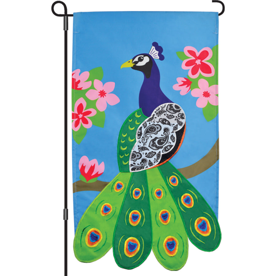 Brightly embroidered 13 in. Enhanced Flag featuring a paisley peacock design, elegantly displayed on a standard garden flag pole in a flourishing garden.