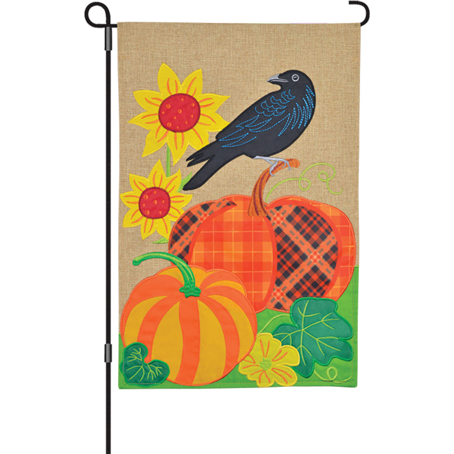 13 in. Enhanced Flag - Pumpkin Crow with detailed embroidery of a crow and pumpkin, displayed on a garden flag pole against a seasonal backdrop.