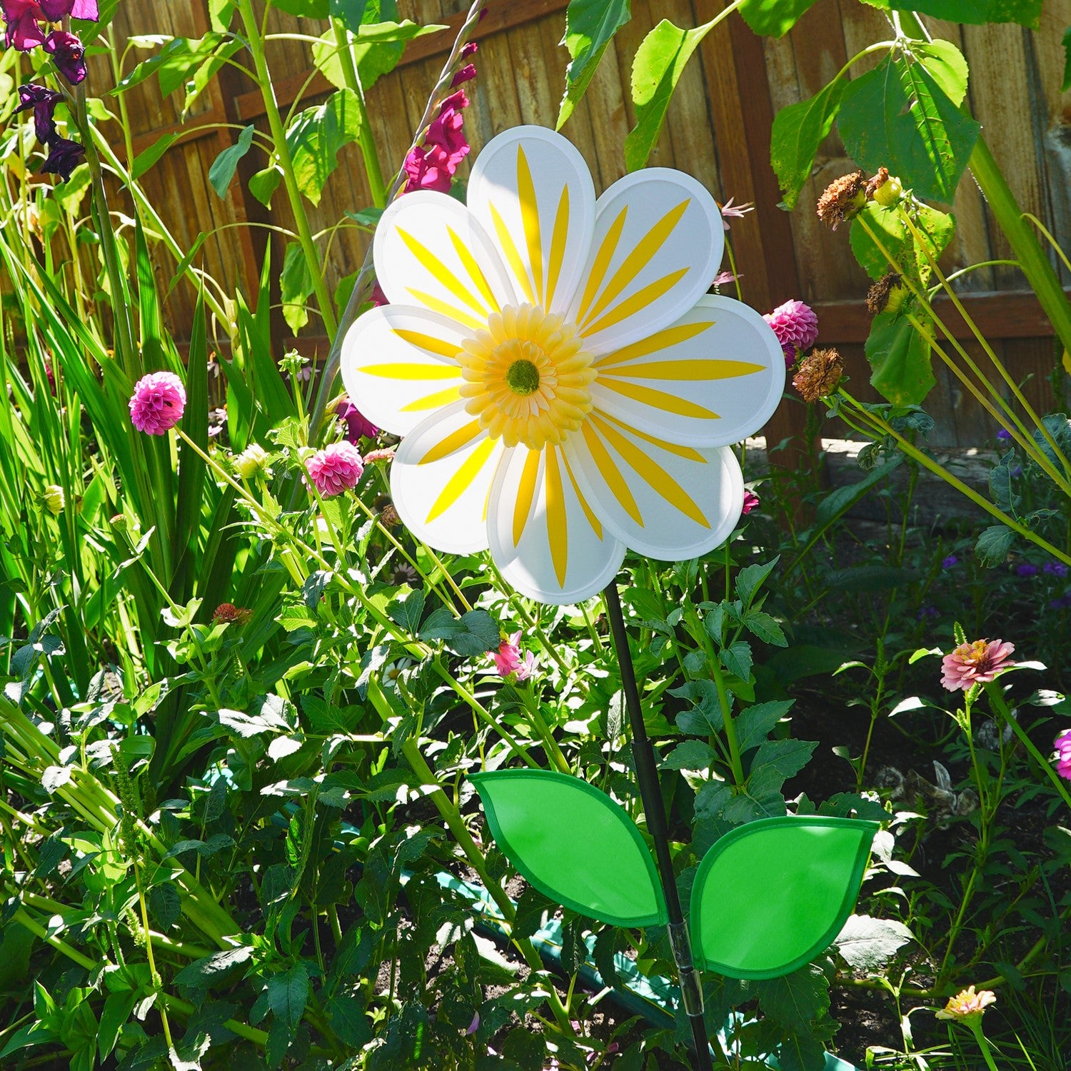 A 13-inch White Daisy Flower Spinner spinning in a garden, featuring an 8-petal design with a white floral motif against a natural backdrop.