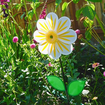 A 13-inch White Daisy Flower Spinner spinning in a garden, featuring an 8-petal design with a white floral motif against a natural backdrop.