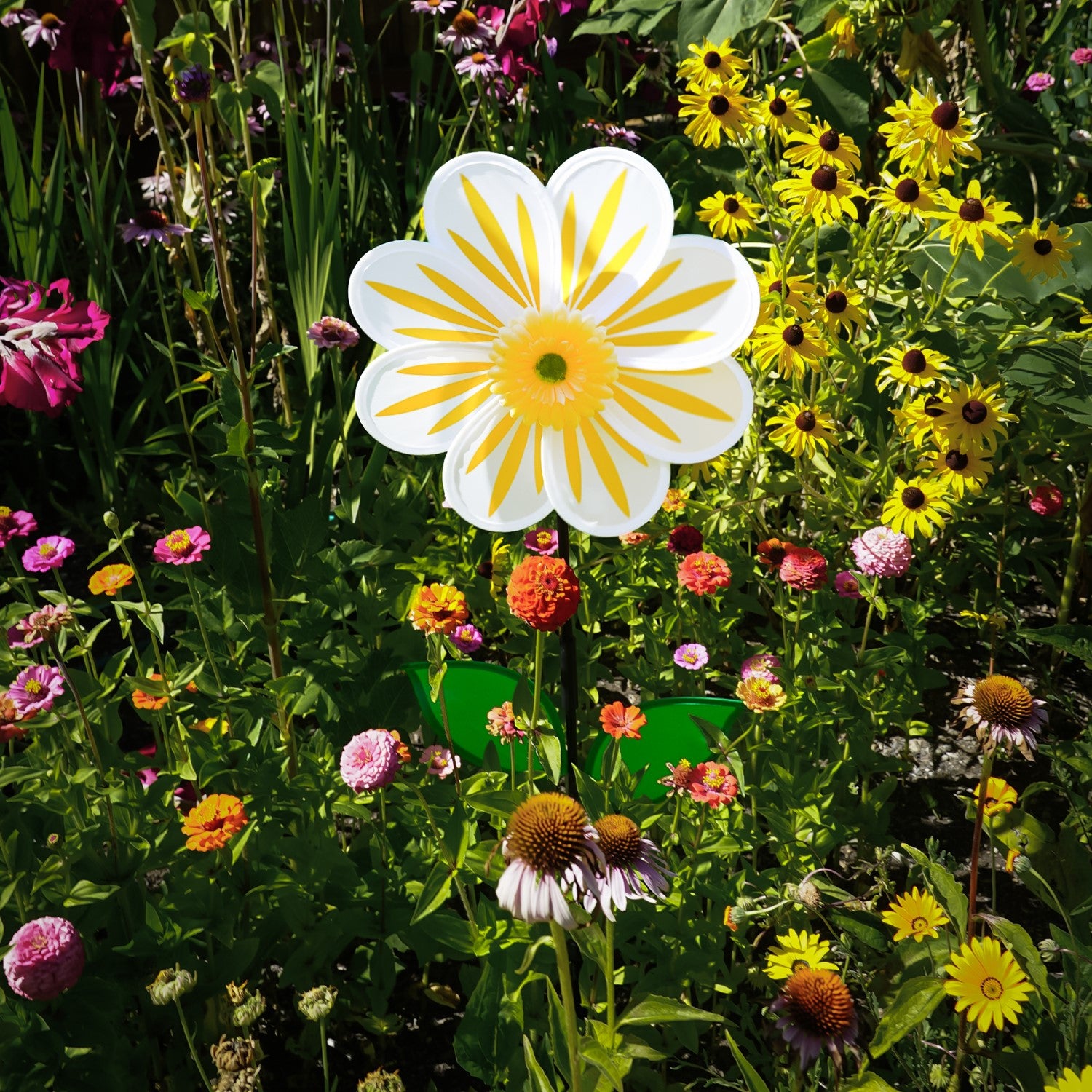 A 13-inch White Daisy Flower Spinner spinning in a garden, featuring an 8-petal design with a white floral motif against a natural backdrop.