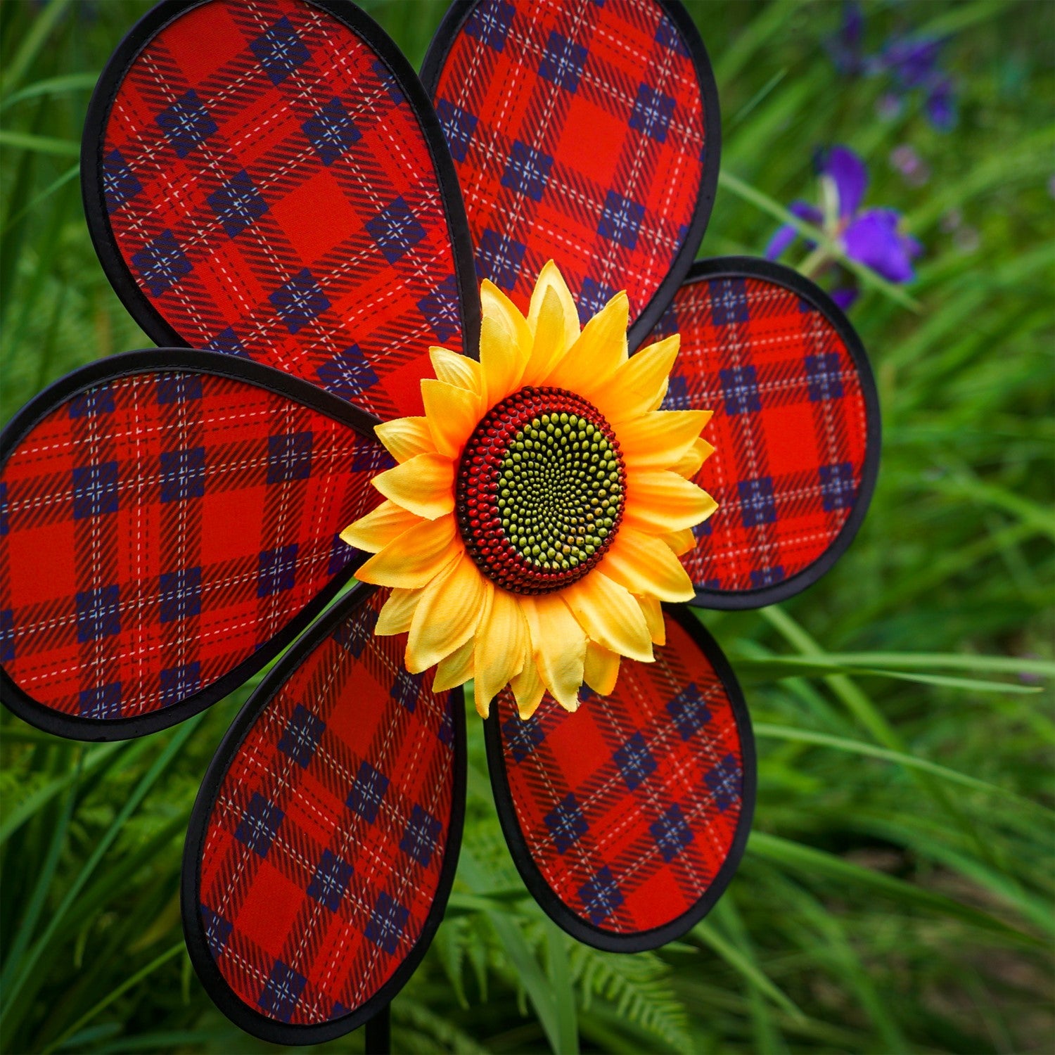 A vibrant 16-inch Red Plaid Flower Spinner with lush green leaves and a sunflower center, rotating gracefully in a garden setting.