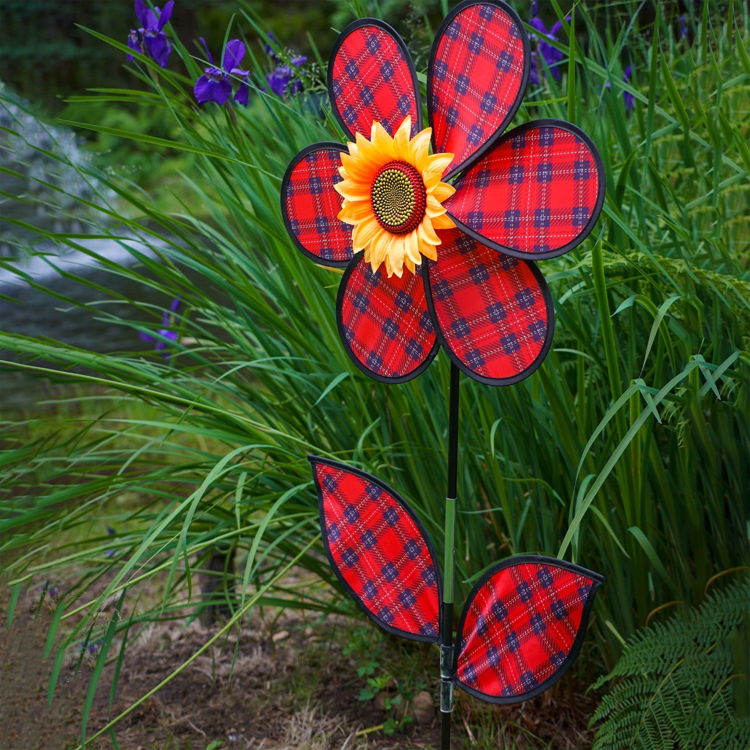 A vibrant 16-inch Red Plaid Flower Spinner with lush green leaves and a sunflower center, rotating gracefully in a garden setting.