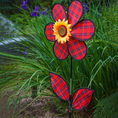 A vibrant 16-inch Red Plaid Flower Spinner with lush green leaves and a sunflower center, rotating gracefully in a garden setting.
