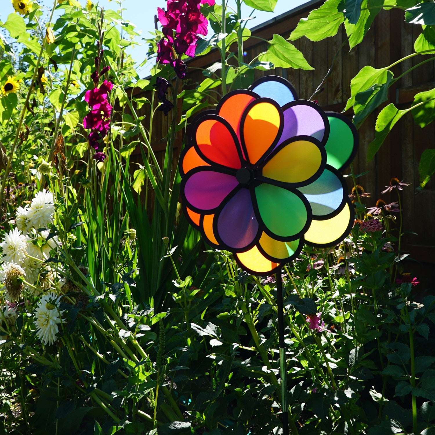18 Petal Triple Flower Spinner with vibrant rainbow colors and rotating flower petals displayed in a garden on a sturdy pole.