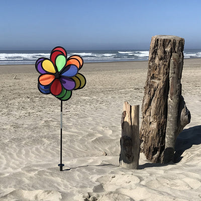 18 Petal Triple Flower Spinner with vibrant rainbow colors and rotating flower petals displayed in a garden on a sturdy pole.