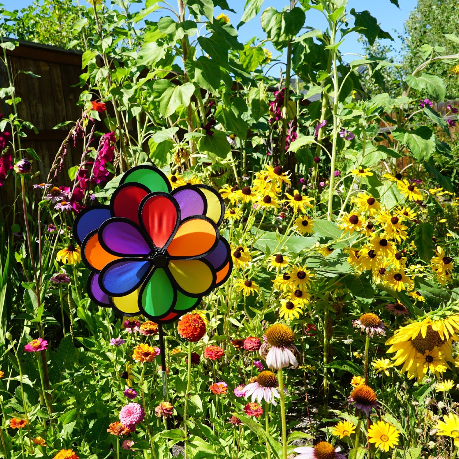 18 Petal Triple Flower Spinner with vibrant rainbow colors and rotating flower petals displayed in a garden on a sturdy pole.