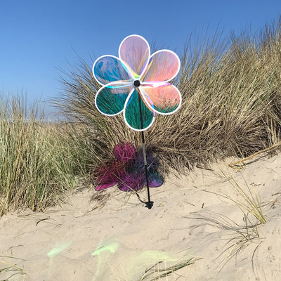 19-inch Iridescent Flower Spinner with transparent Mylar petals captured in a garden setting, reflecting sunlight and colors beautifully.