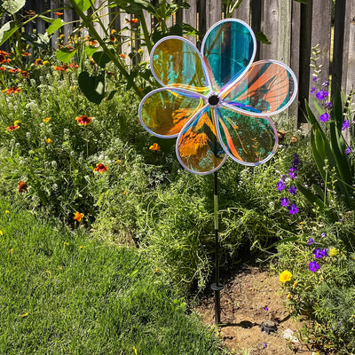 19-inch Iridescent Flower Spinner with transparent Mylar petals captured in a garden setting, reflecting sunlight and colors beautifully.