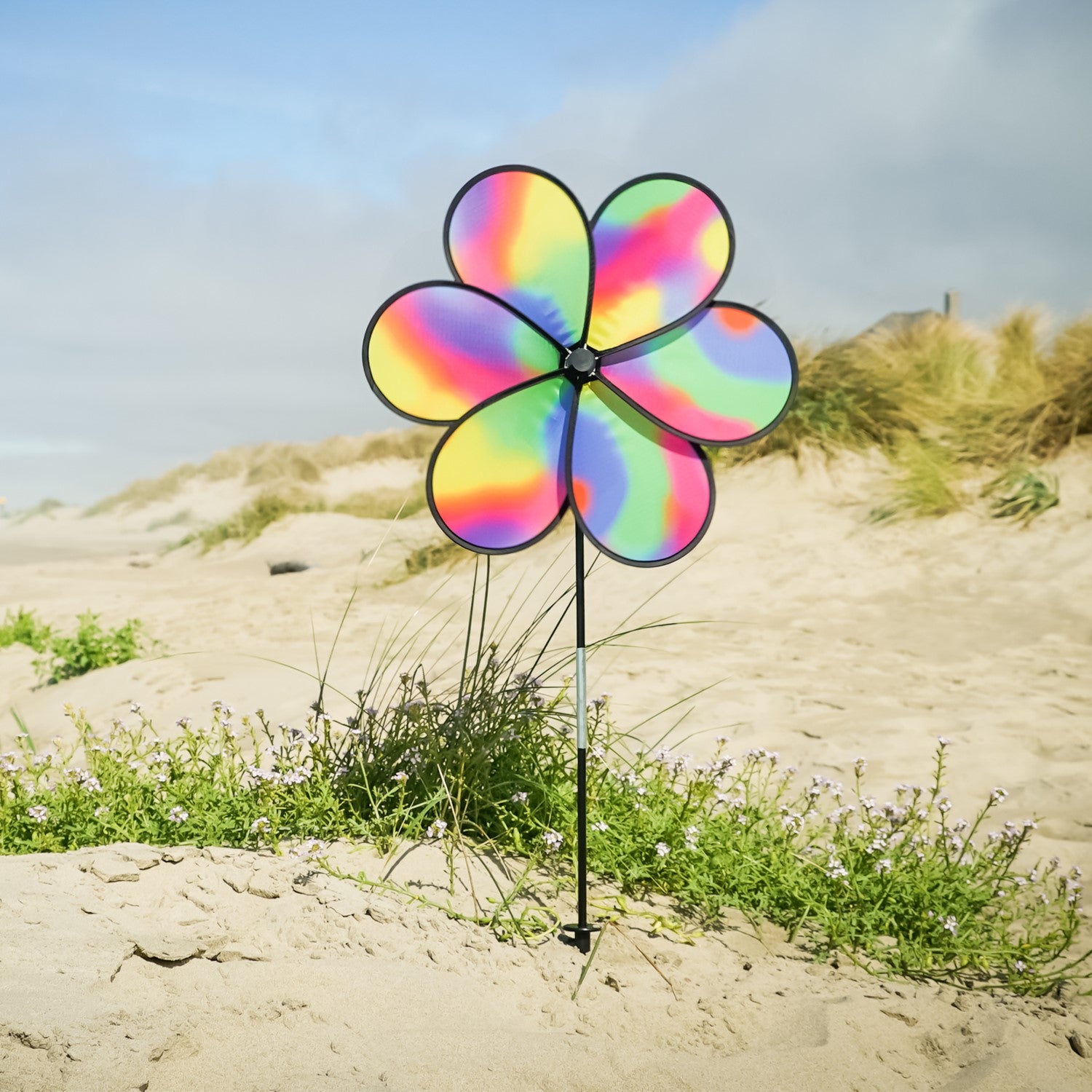19-inch Jewel Flower Spinner with vibrant rainbow flower design, spinning gracefully in a garden setting under bright sunlight.