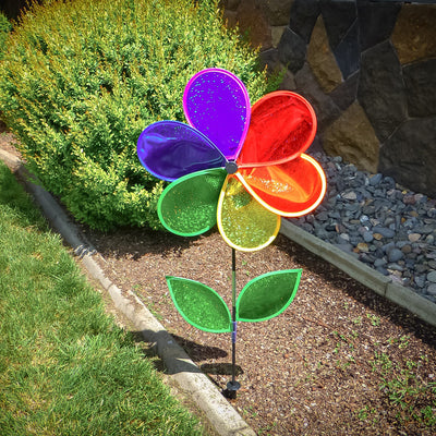 19 inch Rainbow Glitter Flower Spinner with bright Mylar petals spinning on a garden pole in a sunny outdoor yard setting.