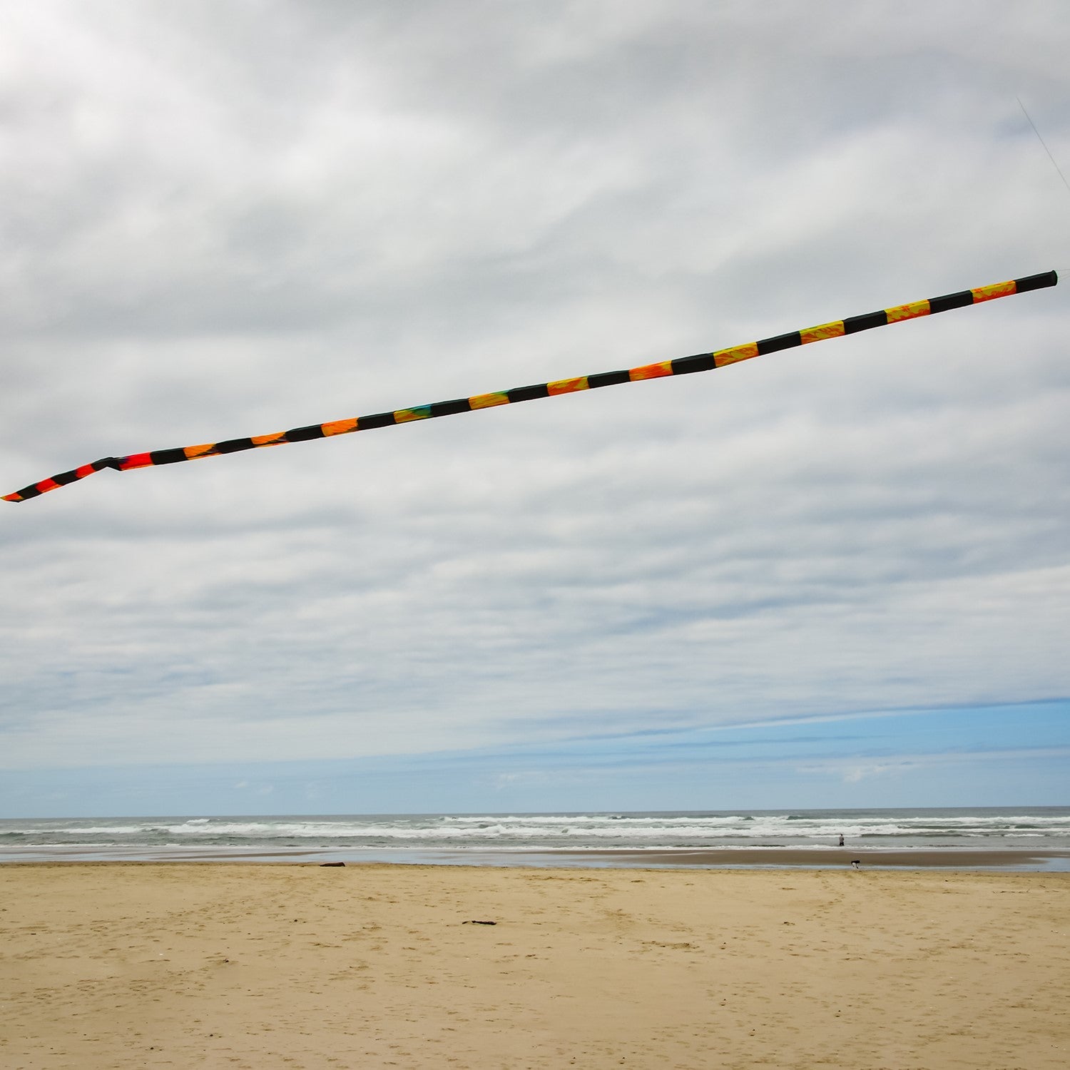 20' Tie Dye & Black Tube Tail with rainbow swirls and black segments soaring in the sky, showcasing its vibrant design and wind-catching capabilities.