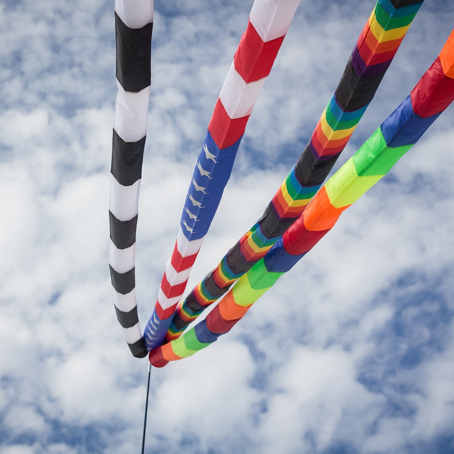 20' Tie Dye & Black Tube Tail with rainbow swirls and black segments soaring in the sky, showcasing its vibrant design and wind-catching capabilities.