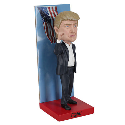 2025 Inauguration Limited Edition Donald Trump Bobblehead featuring a raised fist and American flag backdrop displayed on a shelf.
