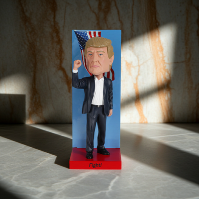 2025 Inauguration Limited Edition Donald Trump Bobblehead featuring a raised fist and American flag backdrop displayed on a shelf.