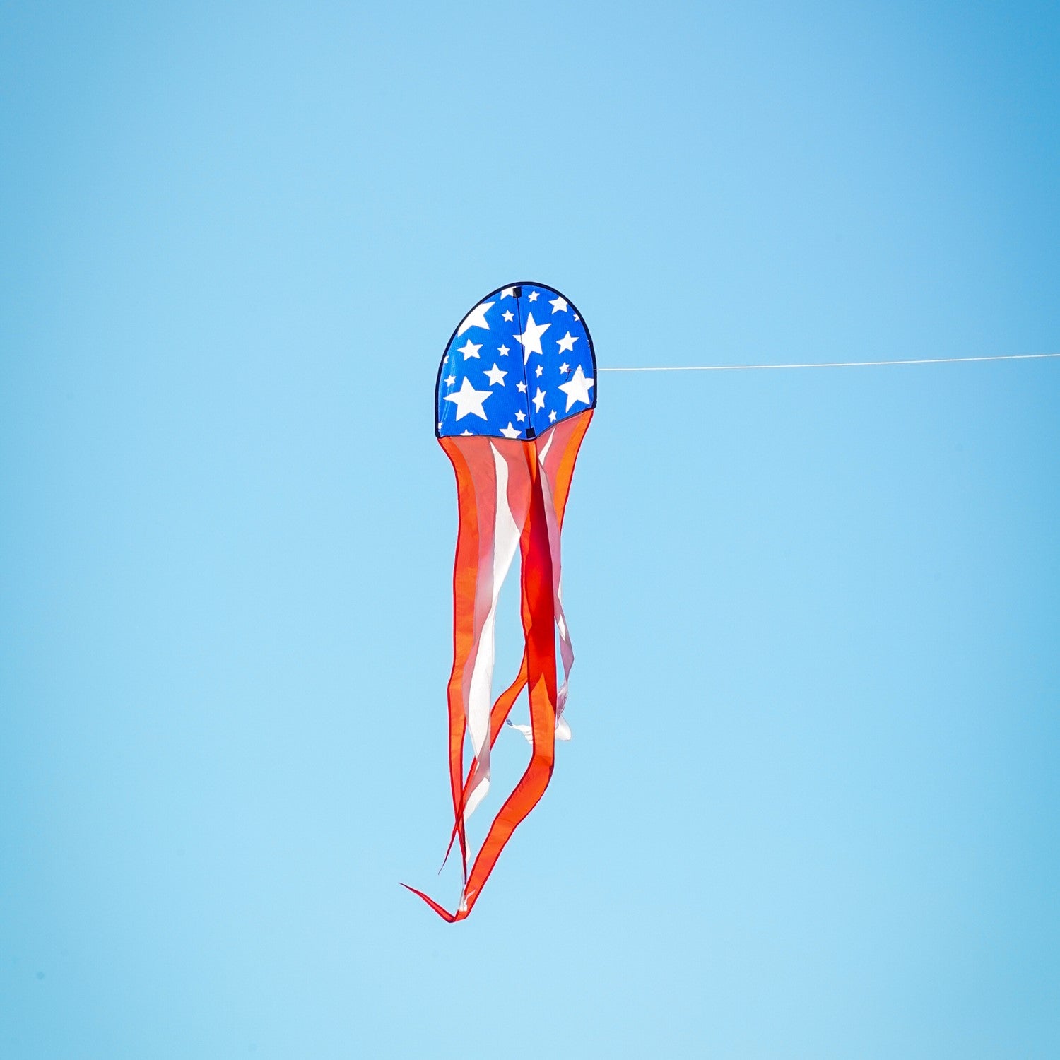 22" Patriot Dancing Dragon Kite with stars and stripes design soaring through the sky during a sunny outdoor event with tails flowing.