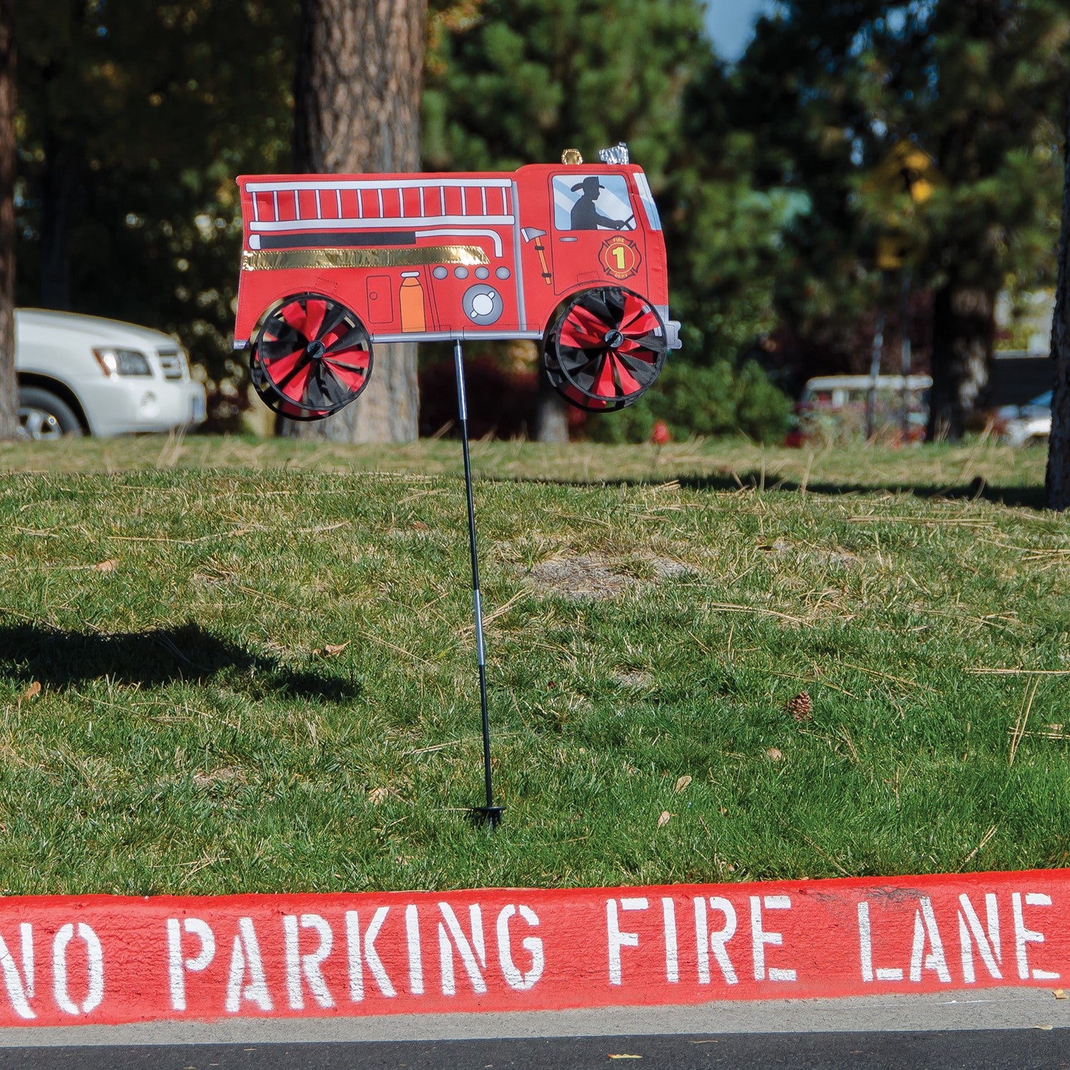 Vibrant 24'' Fire Truck Spinner in a garden setting with spinning wheels, showcasing a charming red fire truck design in motion.