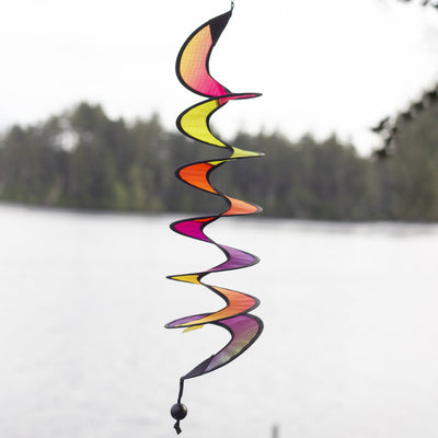 24-inch Jewel Curlie featuring a colorful rainbow graphic, hanging elegantly in an outdoor garden setting, moving gently in the breeze.