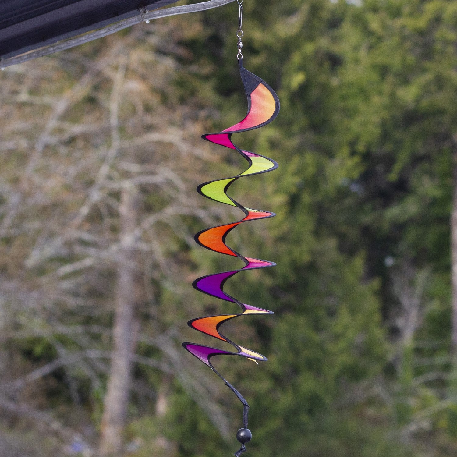 24-inch Jewel Curlie featuring a colorful rainbow graphic, hanging elegantly in an outdoor garden setting, moving gently in the breeze.
