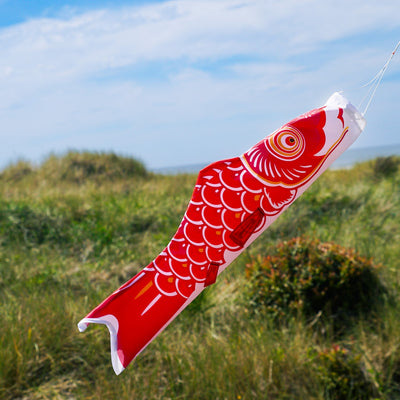 24-inch Red Koi windsock hanging outdoors, featuring a vibrant red koi fish design fluttering in the breeze against a clear sky.