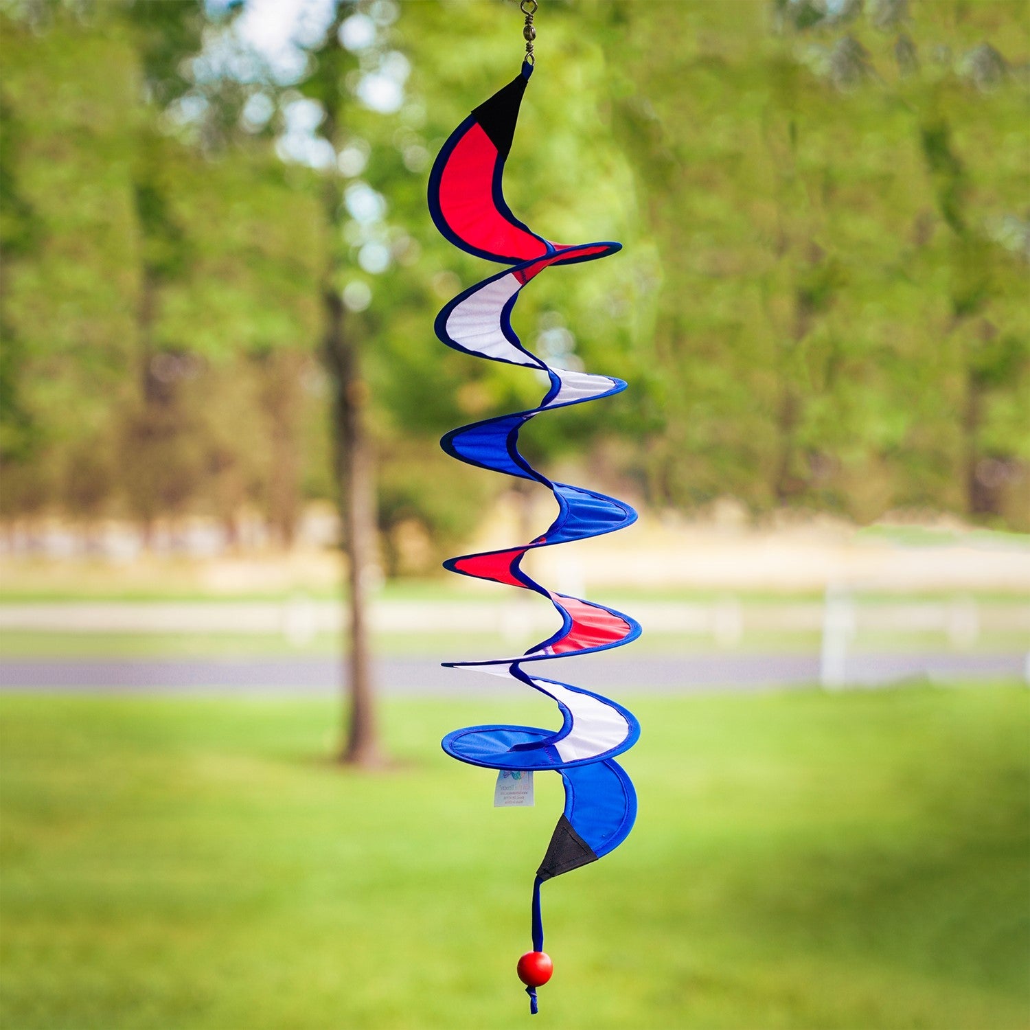 24-inch Red, White and Blue Curlie spinner hanging outdoors, displaying a vibrant spiral design in patriotic colors, gently swirling in the breeze.