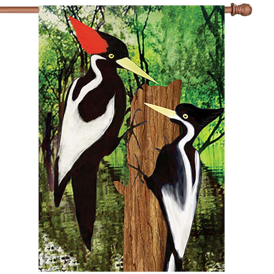 28 in. Ivory Woodpecker garden flag featuring a whimsical woodpecker and autumn leaves displayed on a flag stand in a bright outdoor setting.