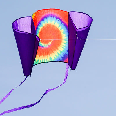 30-inch Tie Dye Sled Kite with purple tails soaring in a clear blue sky, showcasing its vibrant colors and user-friendly design for outdoor fun.