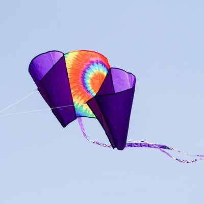 30-inch Tie Dye Sled Kite with purple tails soaring in a clear blue sky, showcasing its vibrant colors and user-friendly design for outdoor fun.