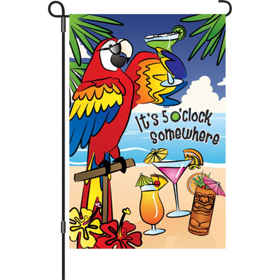 12 In. Flag - 5 O'Clock Somewhere with colorful text displayed outdoors, gently swaying in the wind against a sunny garden backdrop.