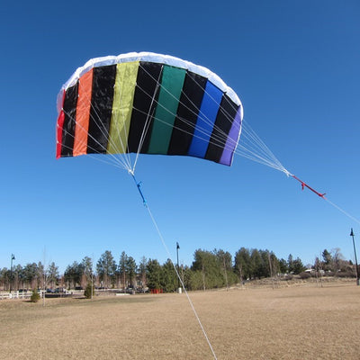 50-inch Sport Air Foil sport kite in rainbow colors, flying against a blue sky with puffy clouds, showcasing its aerodynamic design.