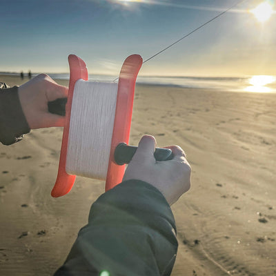 50lb x 500' Braided Breezy WinderTM in coral color with a swivel clip showcased against a clear blue sky, featuring braided kite line.
