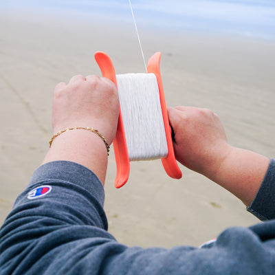 50lb x 500' Braided Breezy WinderTM in coral color with a swivel clip showcased against a clear blue sky, featuring braided kite line.