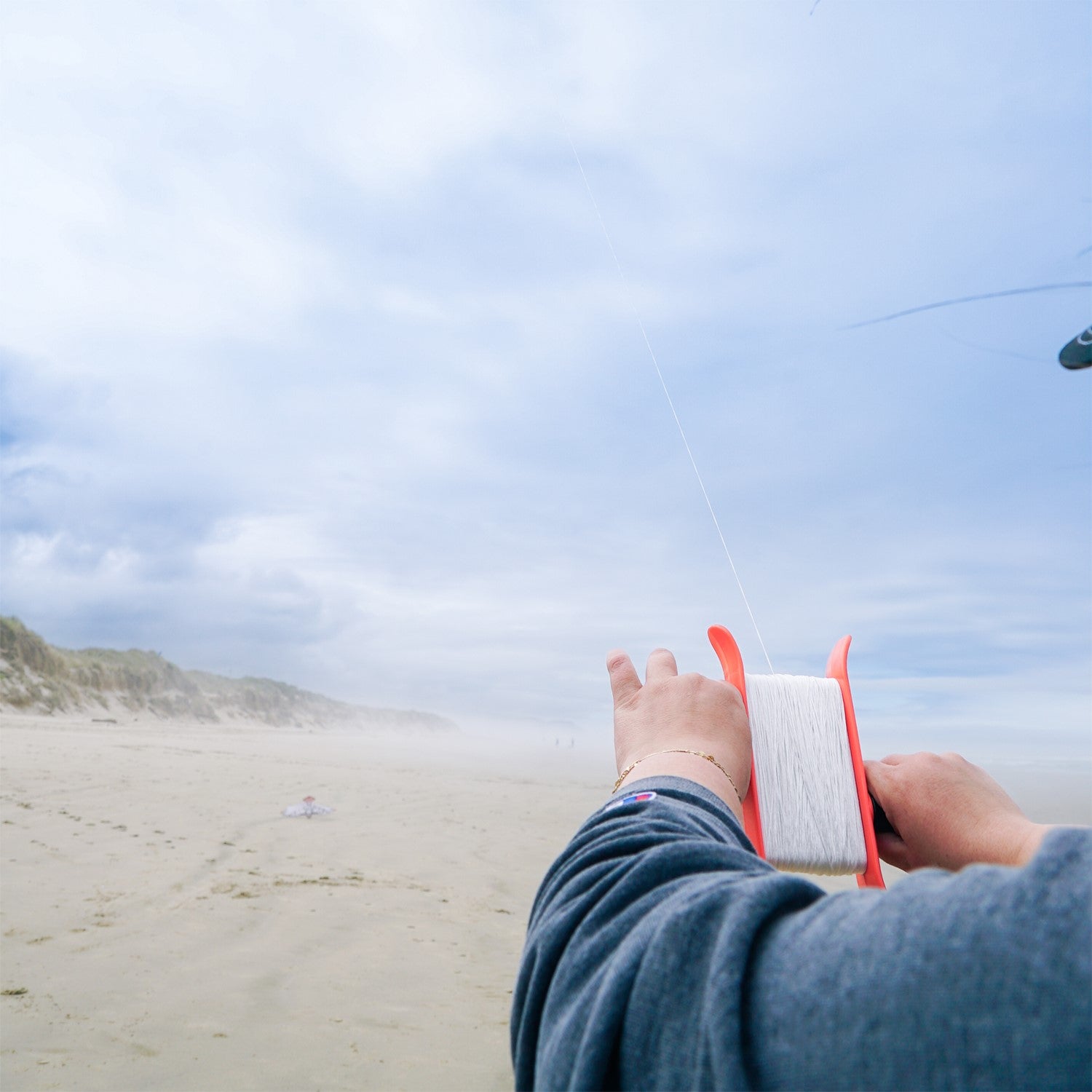 50lb x 500' Braided Breezy WinderTM in coral color with a swivel clip showcased against a clear blue sky, featuring braided kite line.