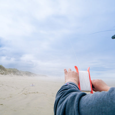 50lb x 500' Braided Breezy WinderTM in coral color with a swivel clip showcased against a clear blue sky, featuring braided kite line.