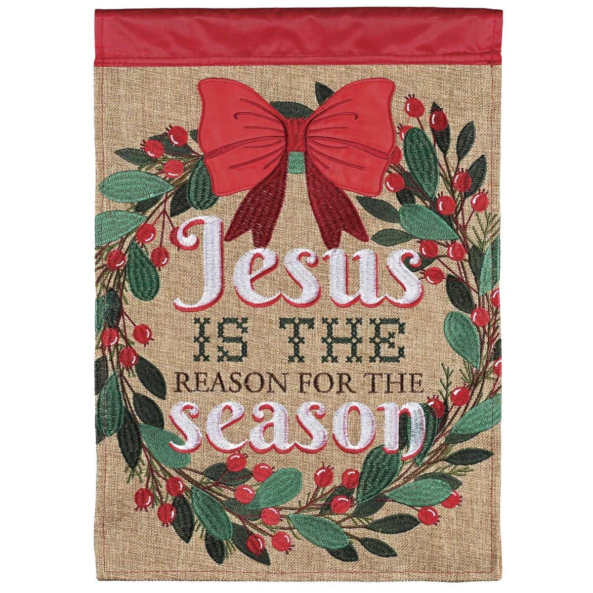 Burlap double applique flag with evergreen wreath and berries surrounding Jesus Is The Reason text, embroidered details, and a pole sleeve ready for outdoor display.